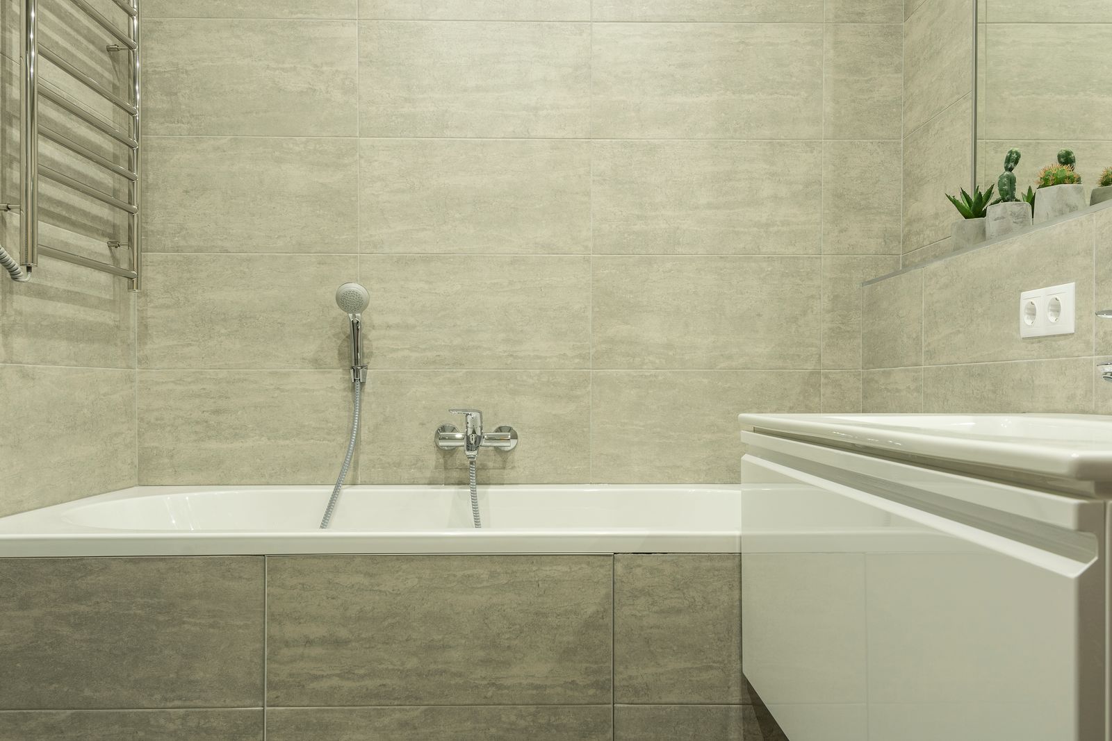 A bathroom with grey tiled walls, a white bathtub and a chrome tap